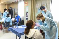 A dental student examines a patient's mouth at a screening, while other students speak with a patient in the background